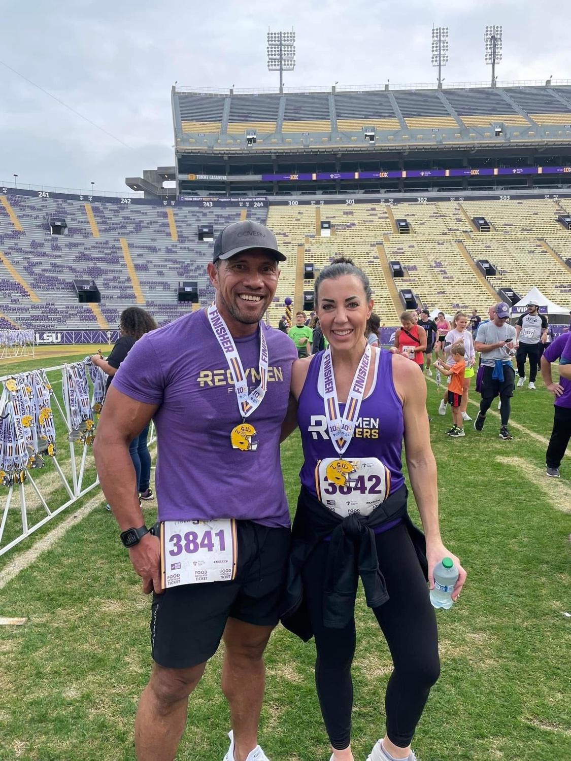 Laie and Emily Wong on the field at LSU Tiger Stadium with finisher medals, wearing Regymen gear
